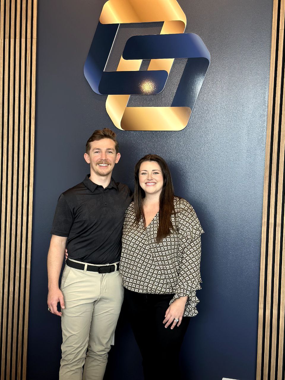 Two dedicated owners from Limitless Chiropractic, your trusted chiropractor in Alliance, standing proudly in their North Fort Worth clinic before the modern gold and blue interconnected C-shape logo.